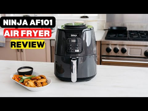 The black Ninja AF101 Air Fryer on a white kitchen countertop, shown next to a plate of cooked chicken wings.