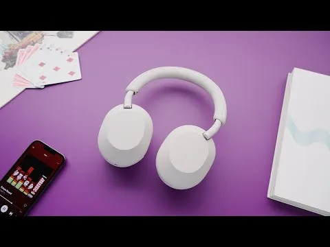 Top-down view of the white Sony WH-1000XM5 headphones on a purple surface next to a smartphone and notebook.
